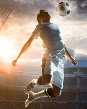 Soccer player jumping to head the ball in stadium with sunset lighting